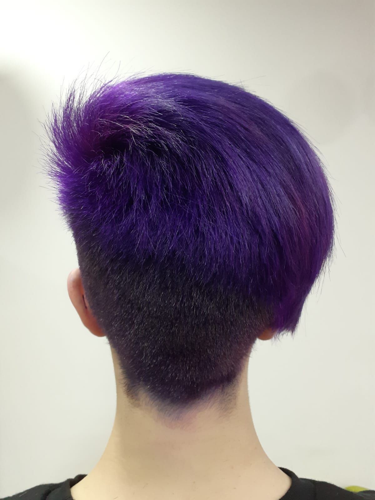 Vista trasera de una persona con el pelo corto de color morado sobre un fondo blanco liso