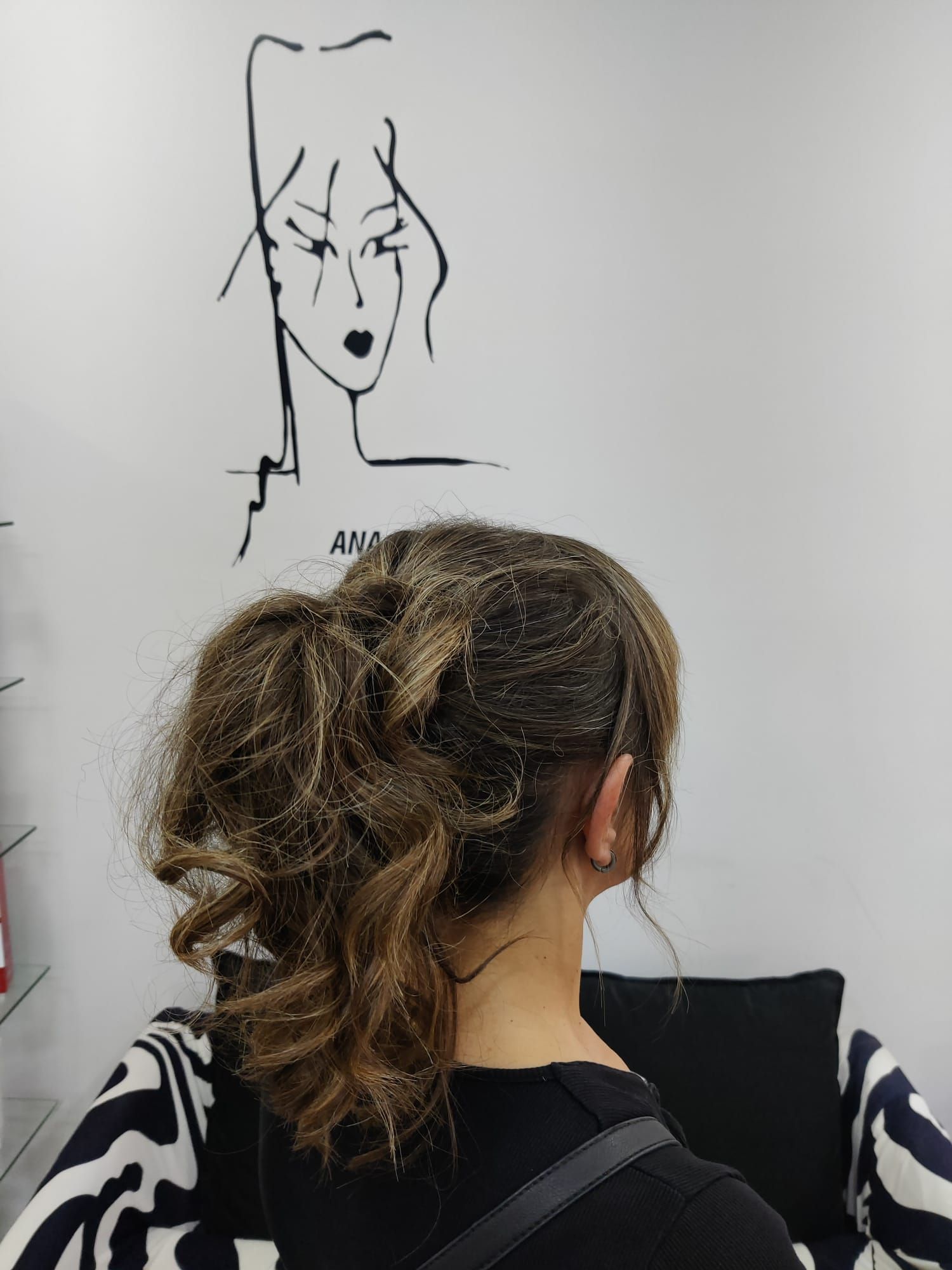 Una persona de cabello castaño y con una prenda blanca y negra está de pie frente a un boceto en la pared de un estudio de arte.