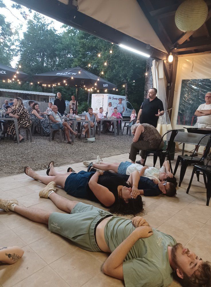 Des personnes sont allongées par terre tandis que d'autres assistent à une présentation en plein air de David Parrat Hypnotiseur.