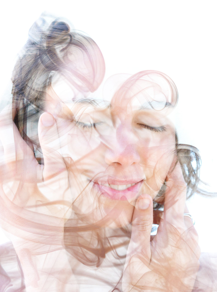 Femme aux yeux fermés, mains près du visage. Fond blanc, avec une fumée aux tons neutres.