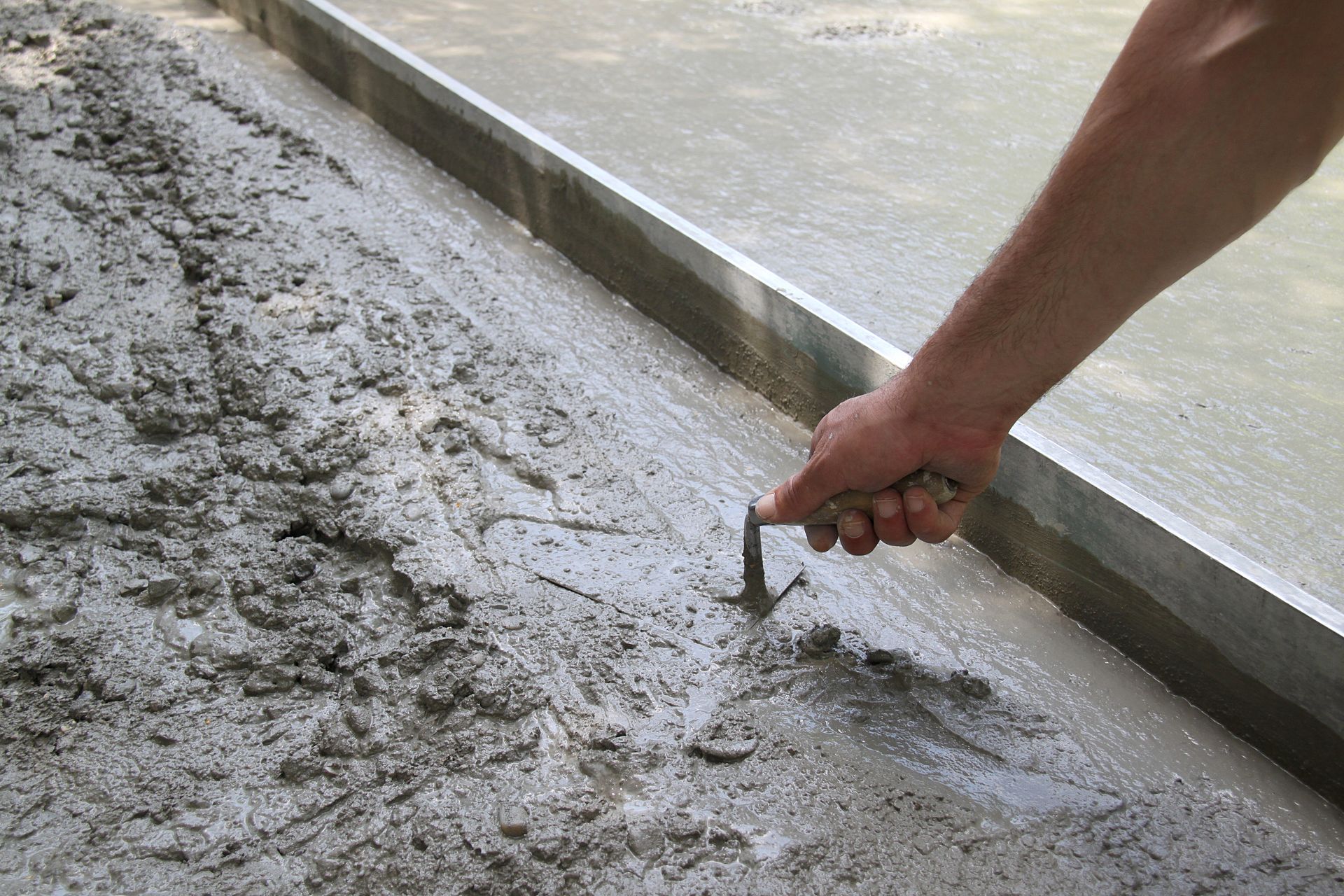 Une personne étale du béton sur le sol avec une truelle.
