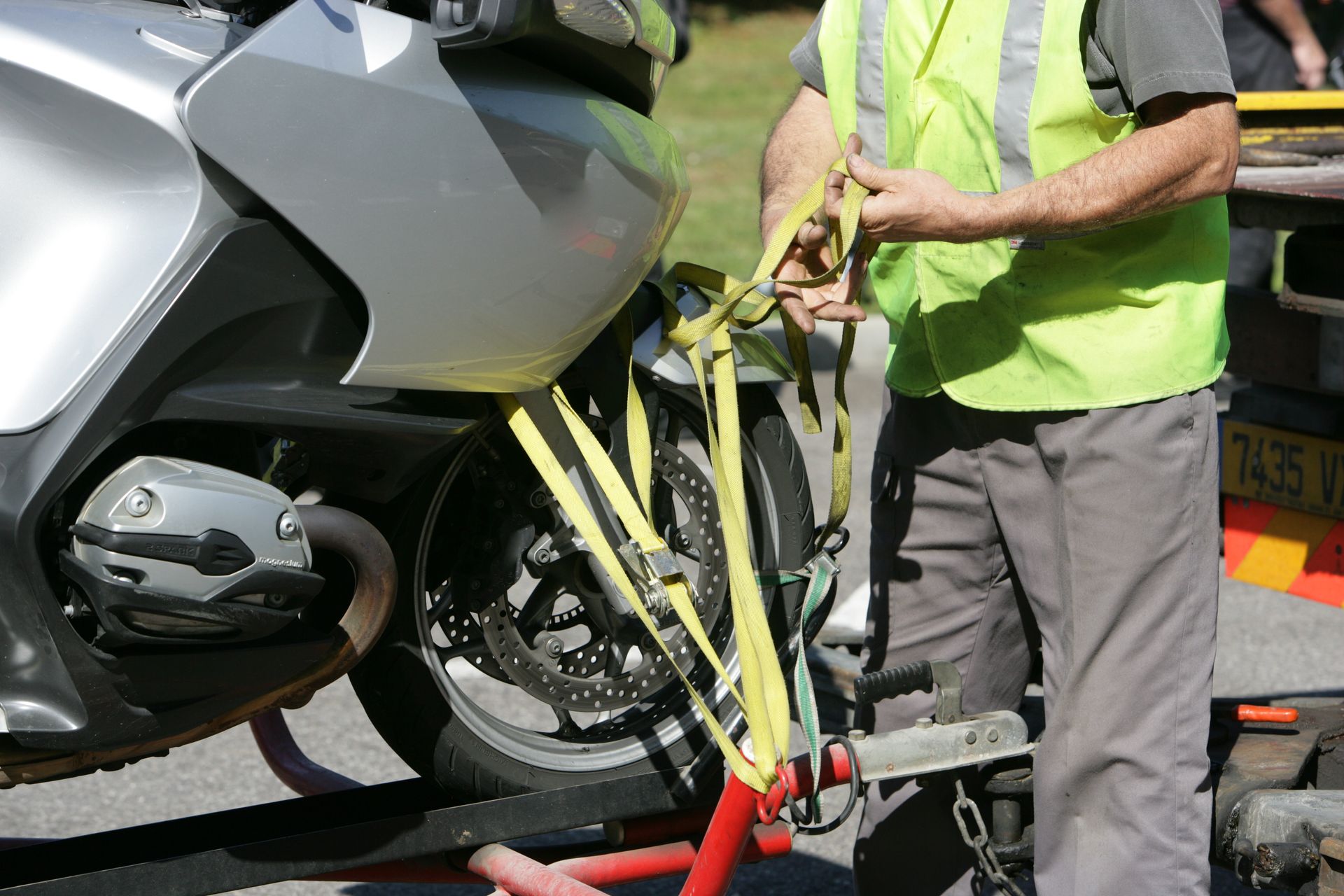Homme portant un gilet jaune en train de fixer avec des sangles la roue avant d'une moto
