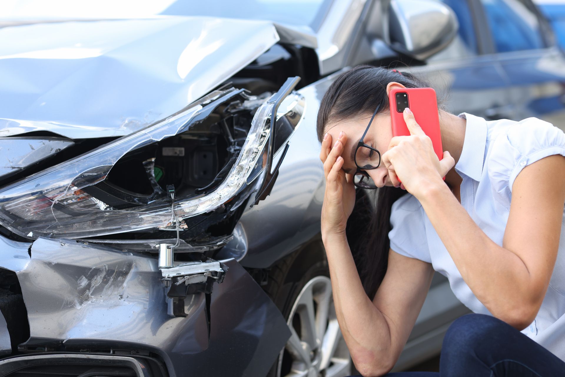 Une femme accroupie au téléphone se tient la tête devant son véhicule endommagé