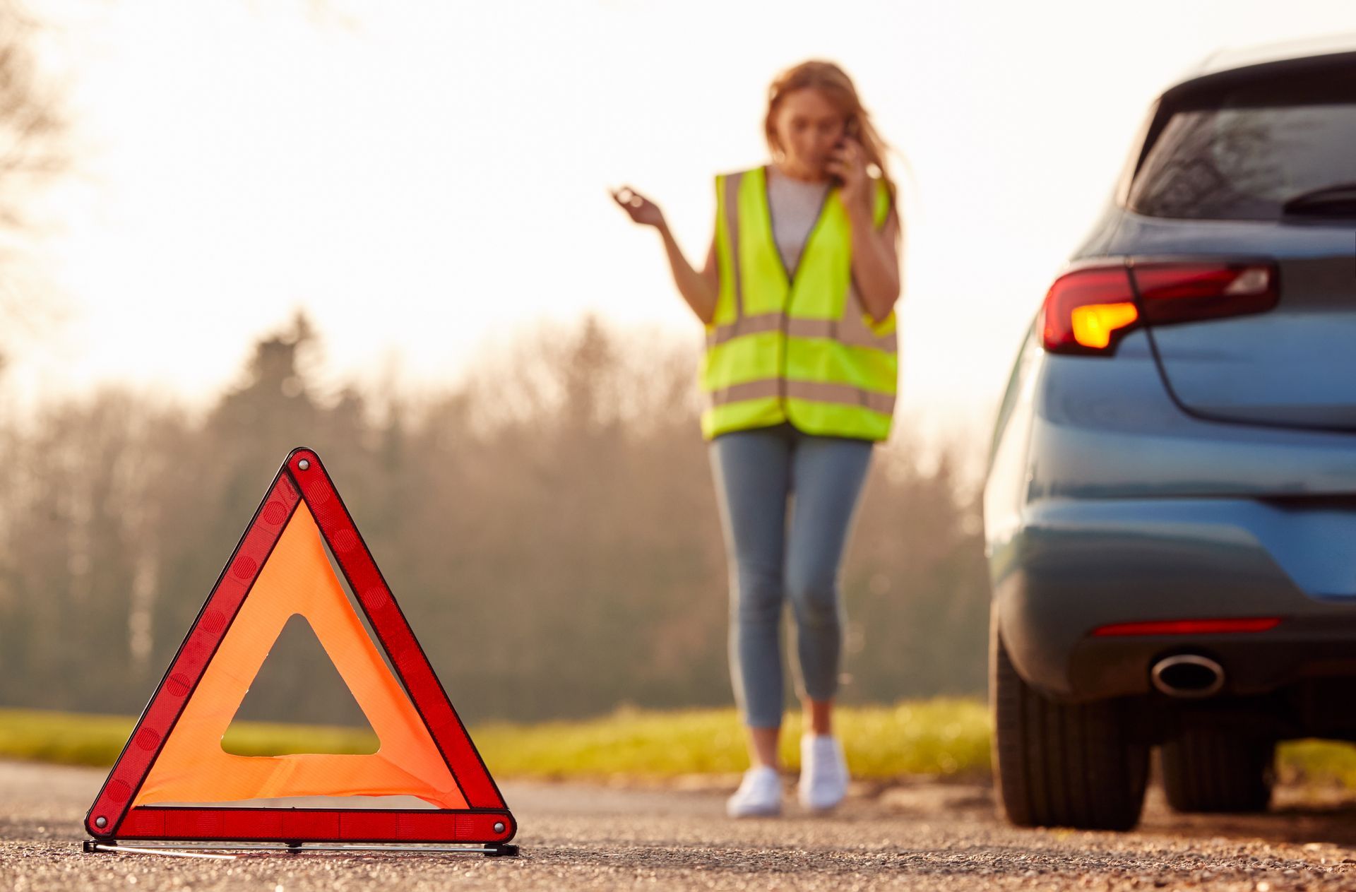 Triangle de signalisation devant une femme en gilet jaune appelant au téléphone à côté de son véhicule