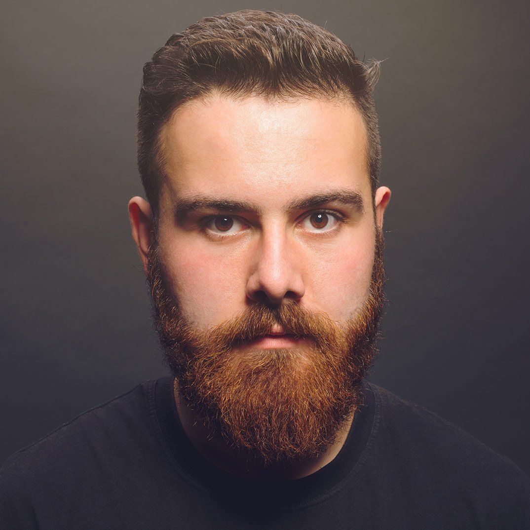 A man with a beard is wearing a black shirt and looking at the camera.