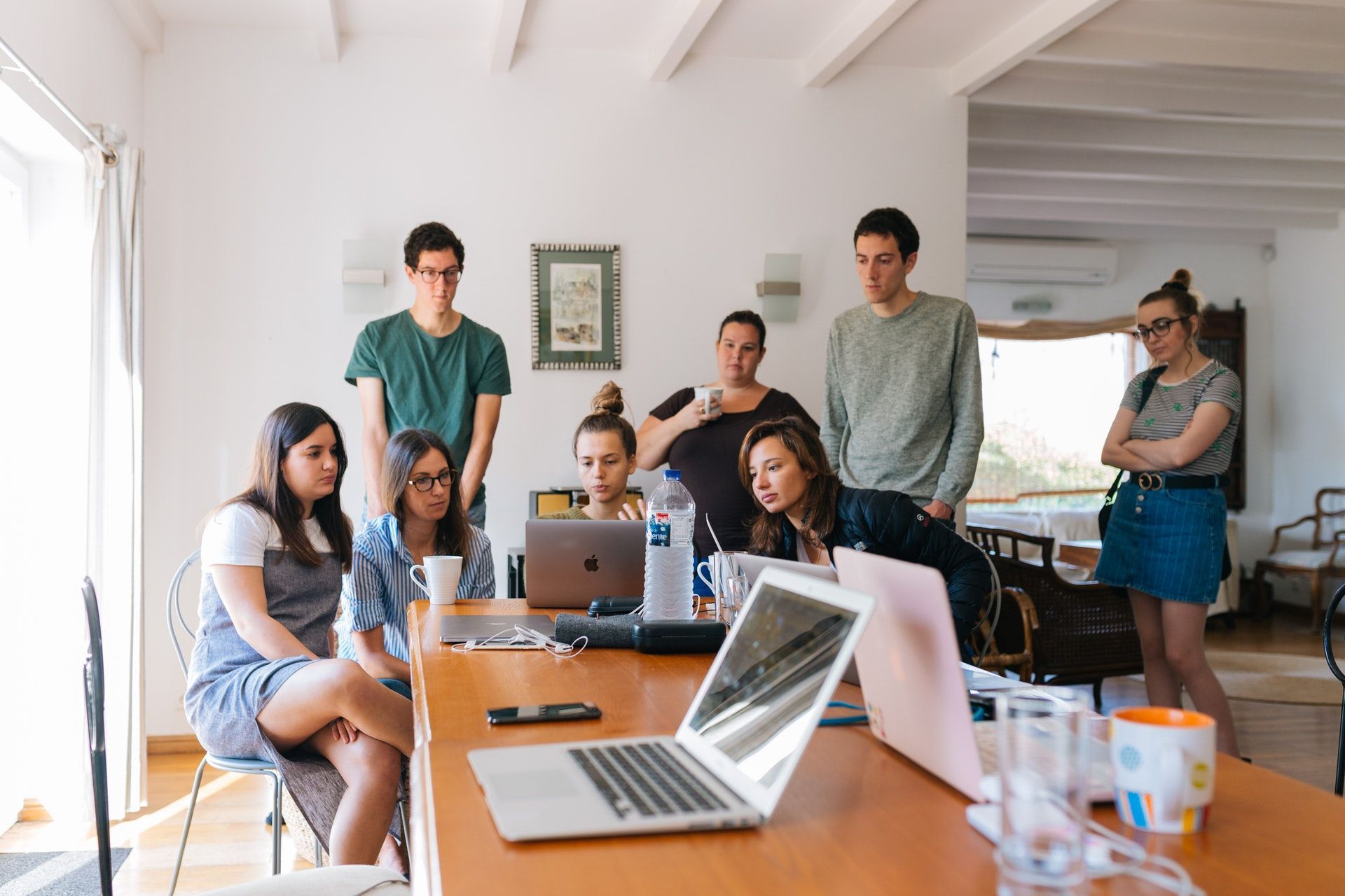 Um grupo de pessoas está sentado ao redor de uma mesa com laptops.