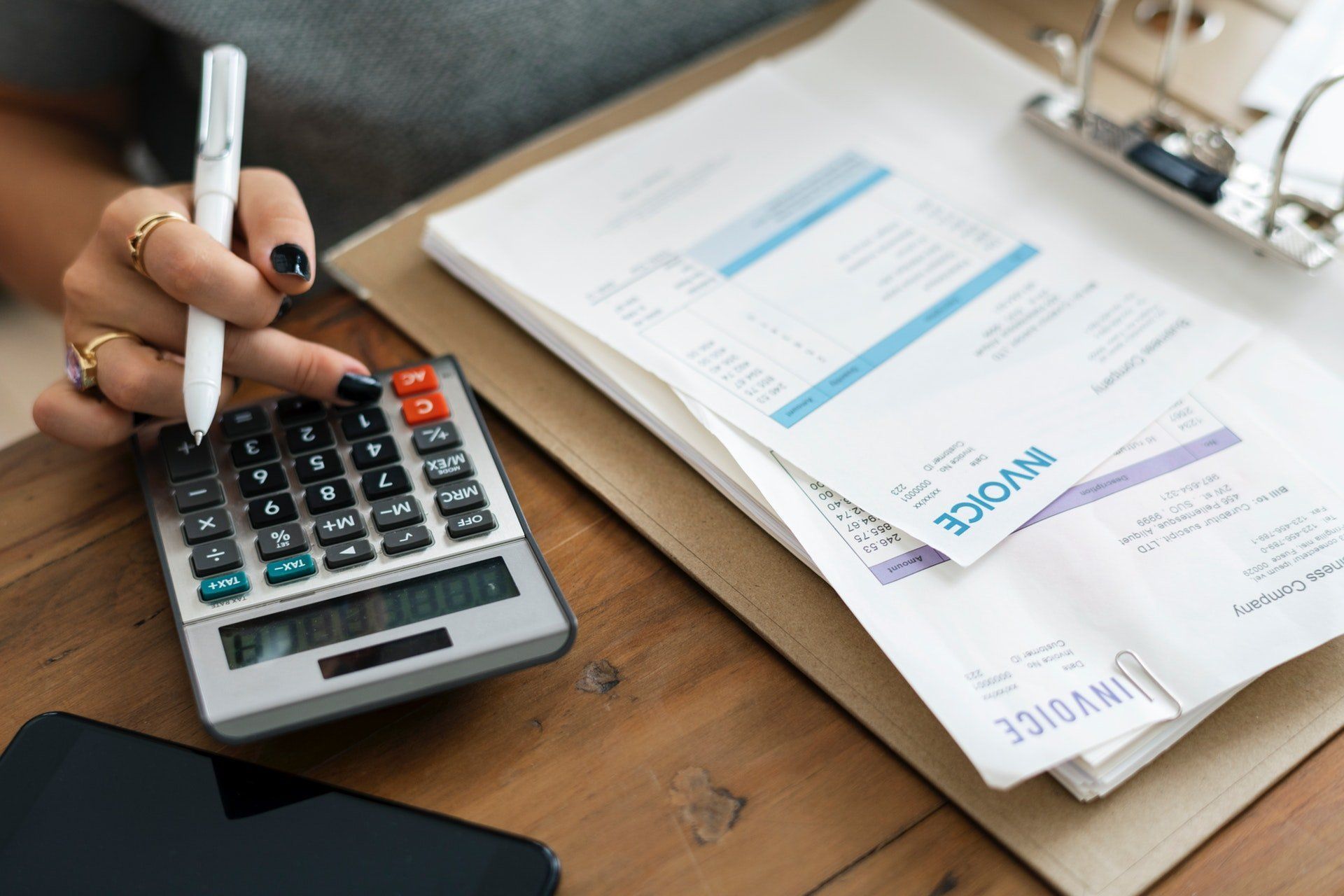 Una mujer está usando una calculadora y escribiendo en un portapapeles.
