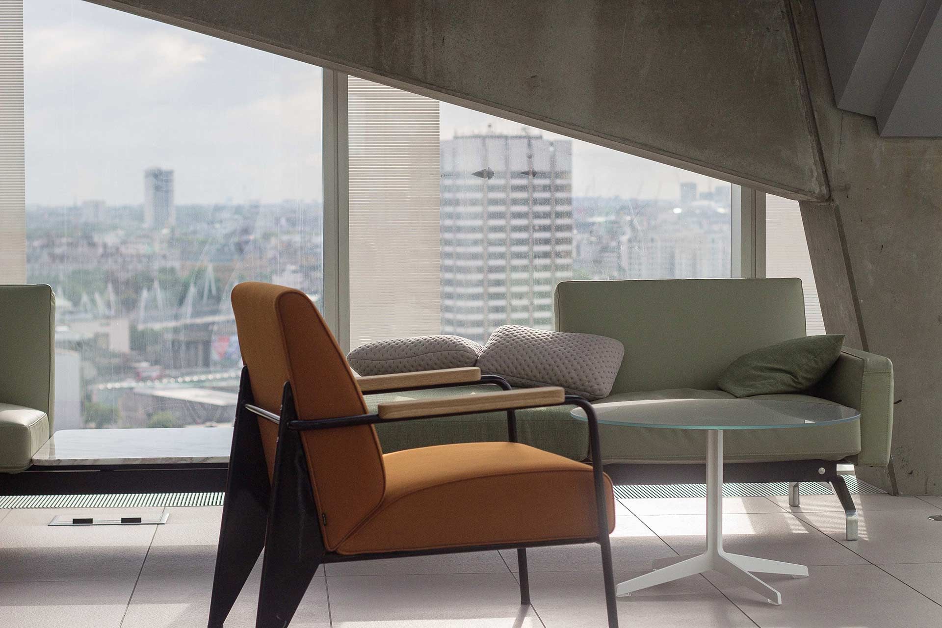 Uma área de estar moderna com uma poltrona laranja, um sofá verde-claro e uma mesa com tampo de vidro com vista