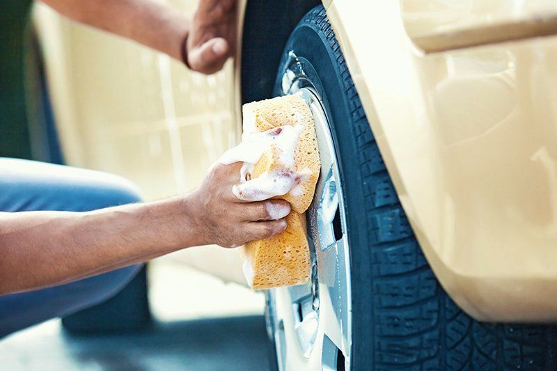 Person, die einen Autoreifen mit einem Seifenschwamm wäscht.