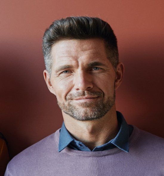 A man with a beard is wearing a purple sweater and smiling.