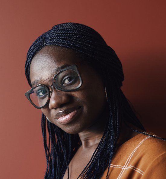A woman wearing glasses and braids is smiling for the camera.