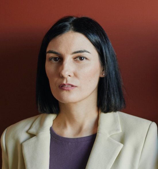 A woman wearing a white jacket and a purple shirt is looking at the camera.