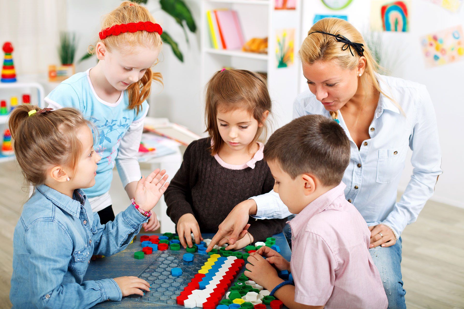 Kinder und Lehrer bauen gemeinsam mit bunten Bauklötzen an einem Tisch im Klassenzimmer.