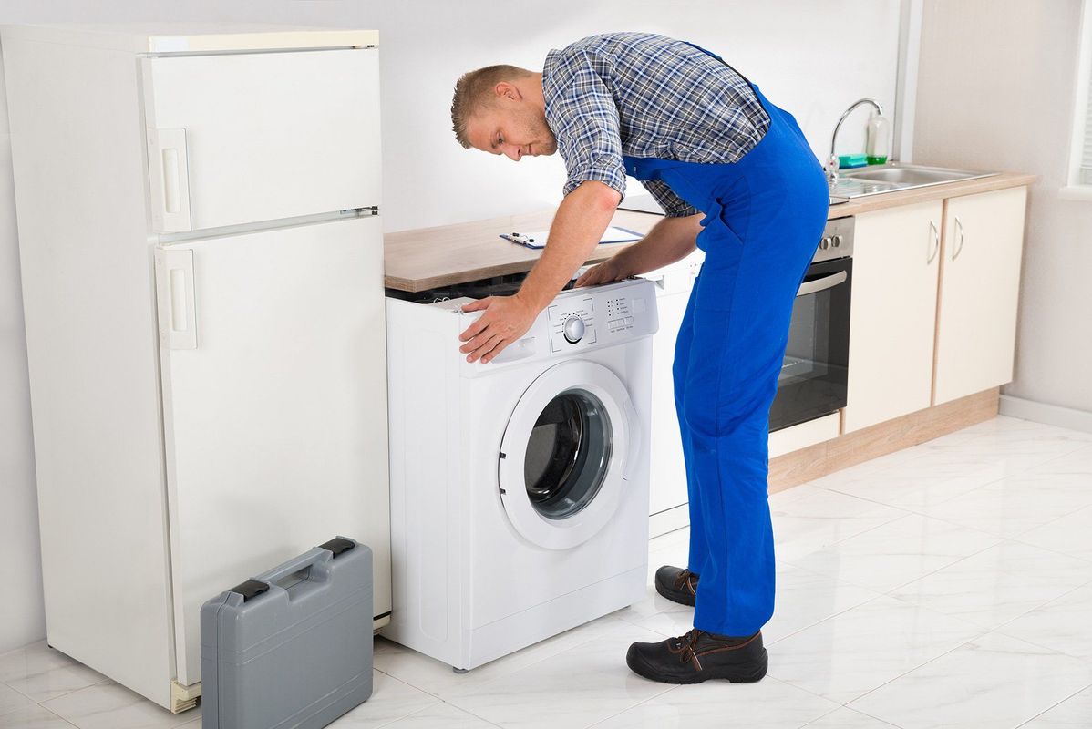 Un hombre está trabajando en una lavadora en una cocina.