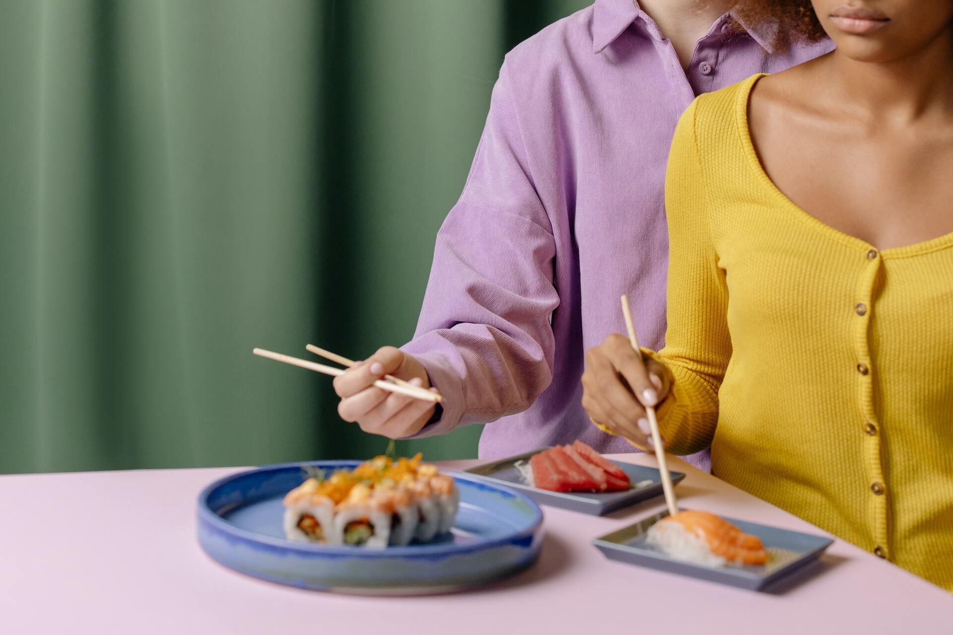 Un hombre y una mujer están sentados en una mesa comiendo sushi con palillos.