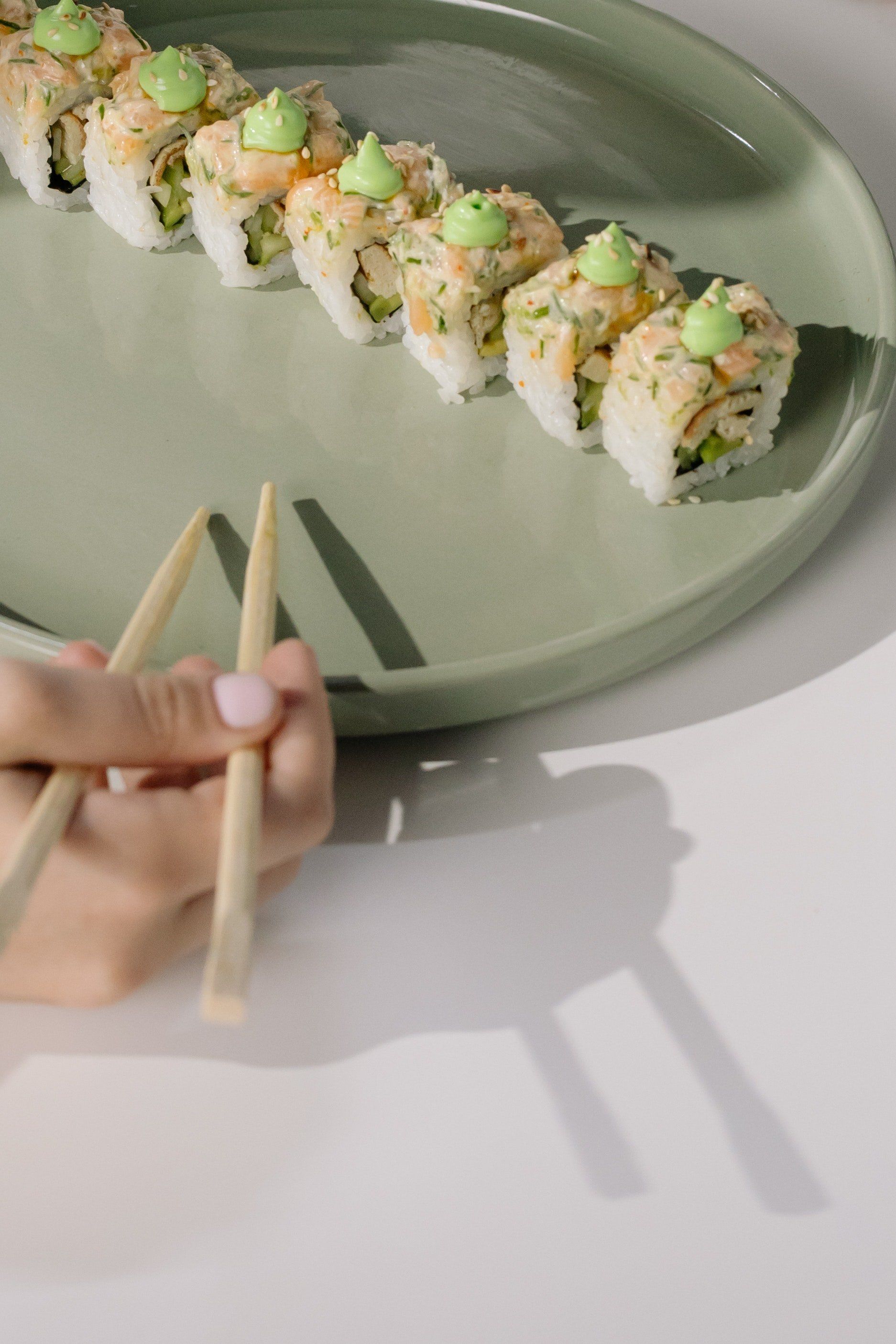 Una persona sostiene palillos delante de un plato de sushi.