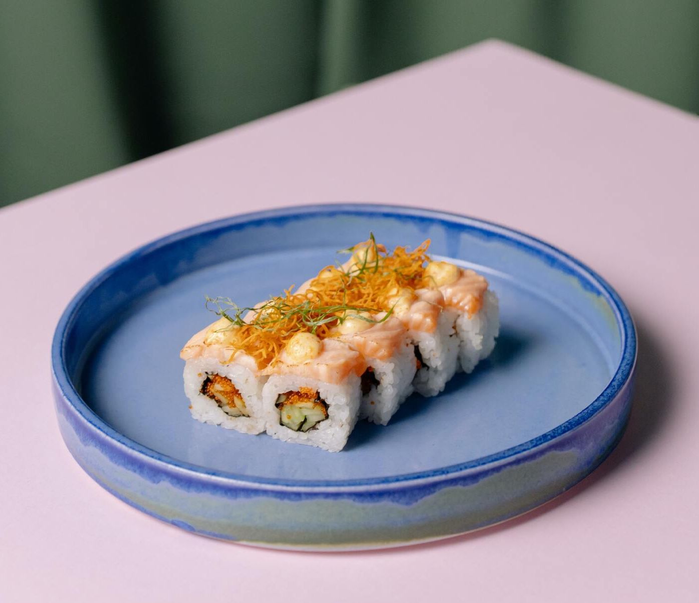 Un plato azul cubierto de sushi sobre una mesa rosa.