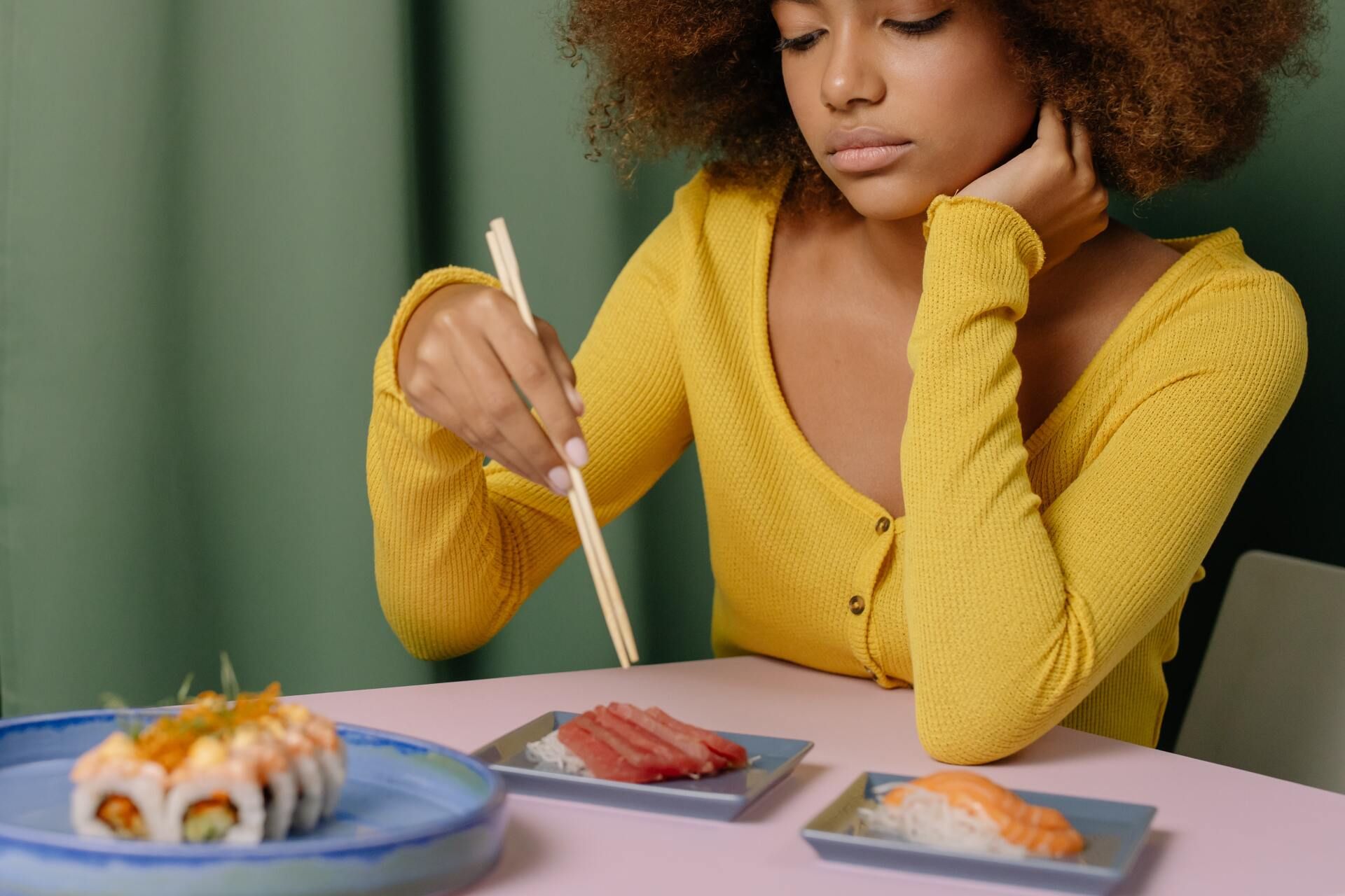Una mujer está sentada en una mesa comiendo sushi con palillos.
