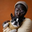 Persona con gafas y gorro sosteniendo un gato blanco y negro sobre un fondo naranja.