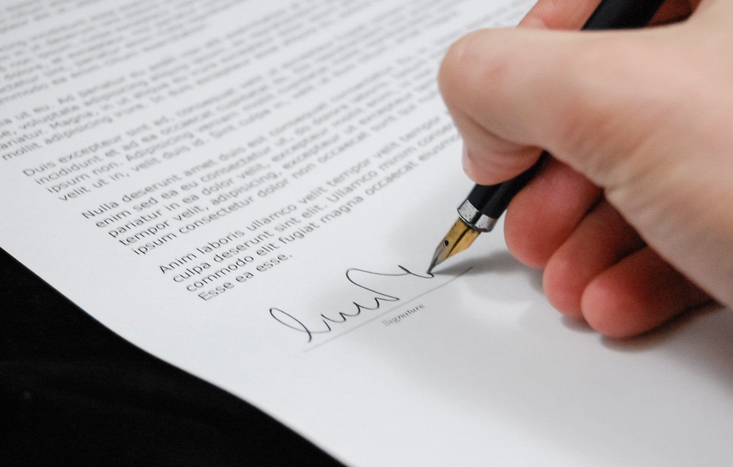 Hand mit Stift beim Unterschreiben eines Dokuments.