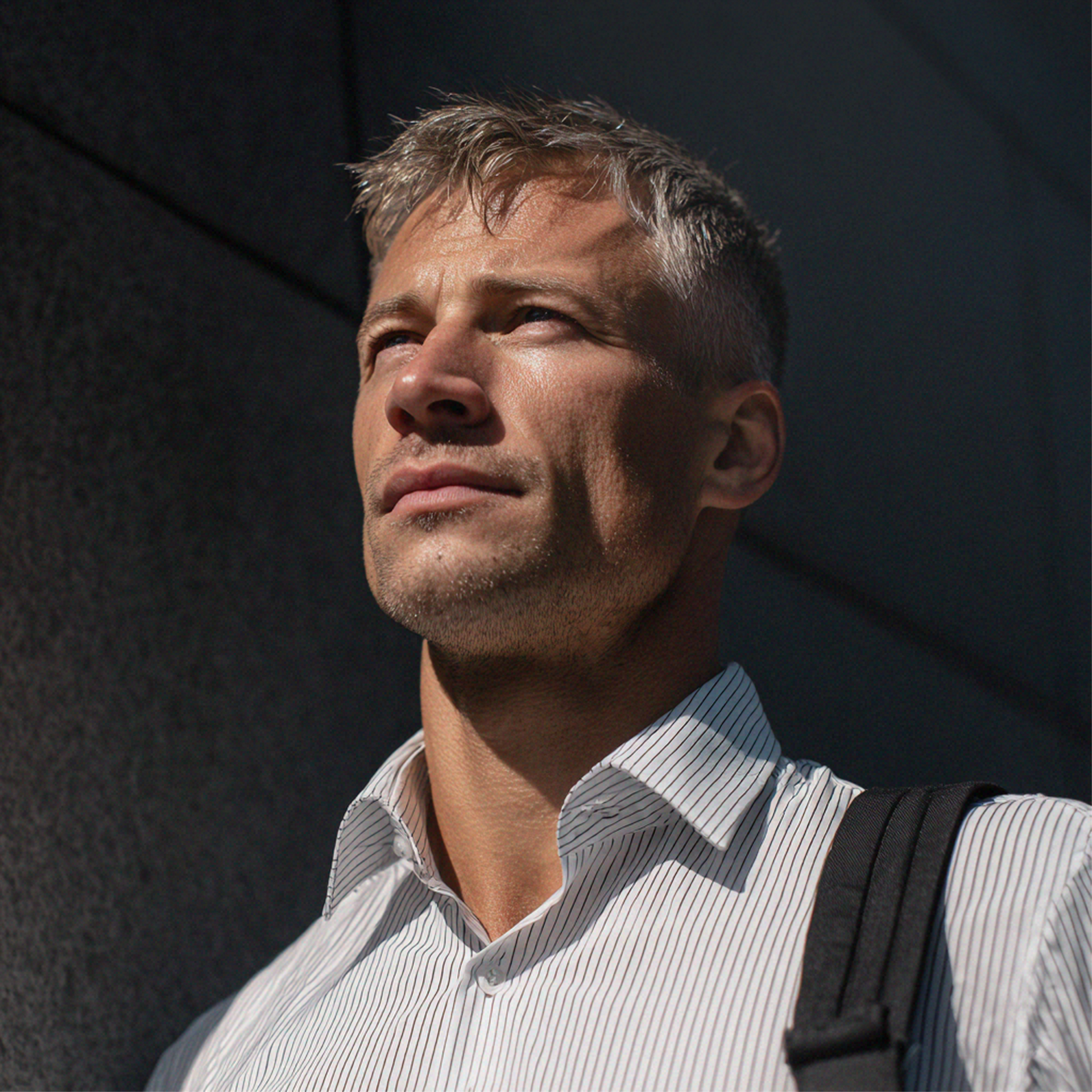 Un homme aux cheveux gris courts, vêtu d'une chemise à rayures et portant un sac à dos