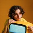 Un joven sostiene un televisor amarillo en sus manos.