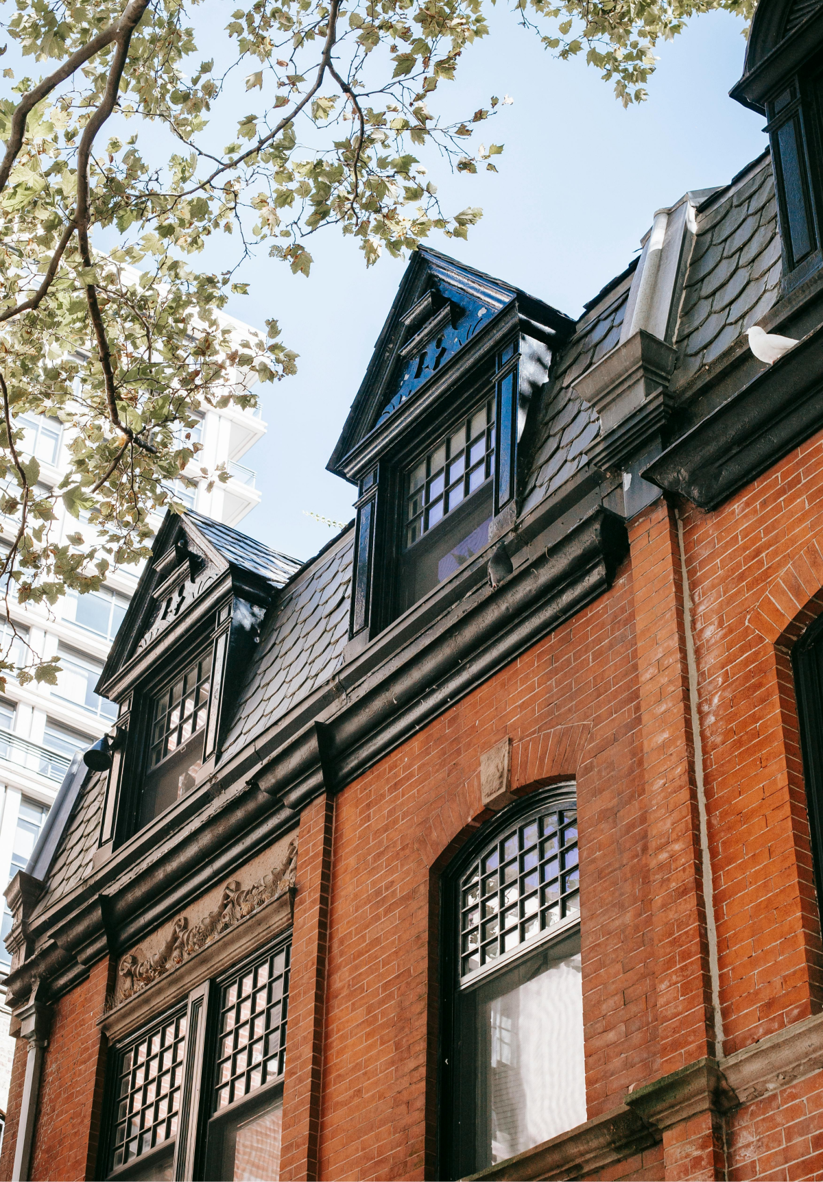Red brick building with dark gray roof, featuring multiple dormer windows, under a blue sky.