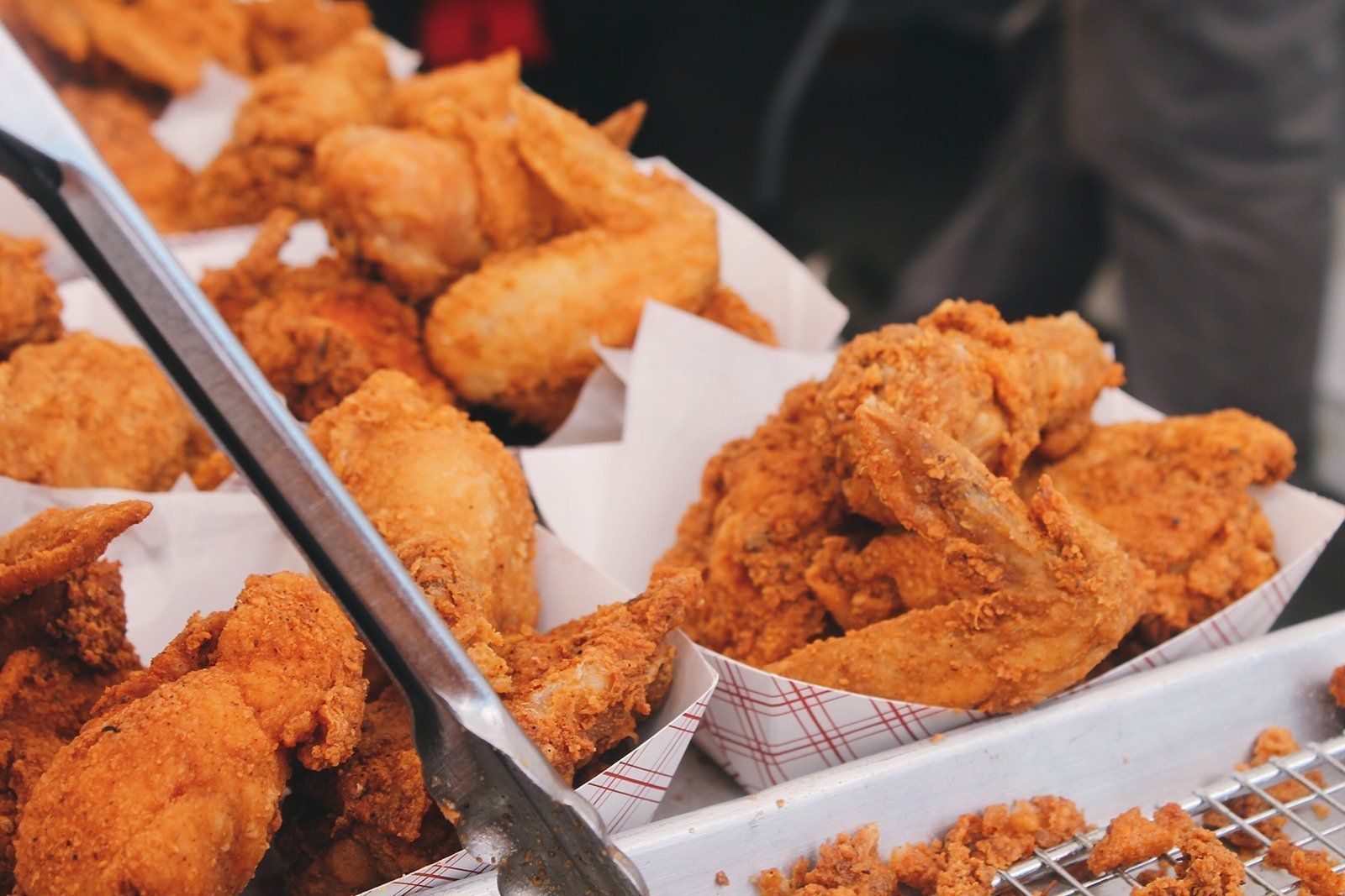 Ein Tablett mit frittierten Hähnchenflügeln und Nuggets mit Zange.