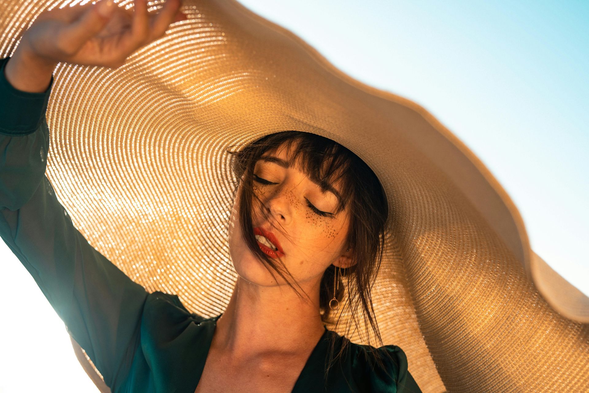 Femme sous un large chapeau de paille, baignée par une douce lumière du soleil, les yeux fermés, vêtue d'un haut turquoise