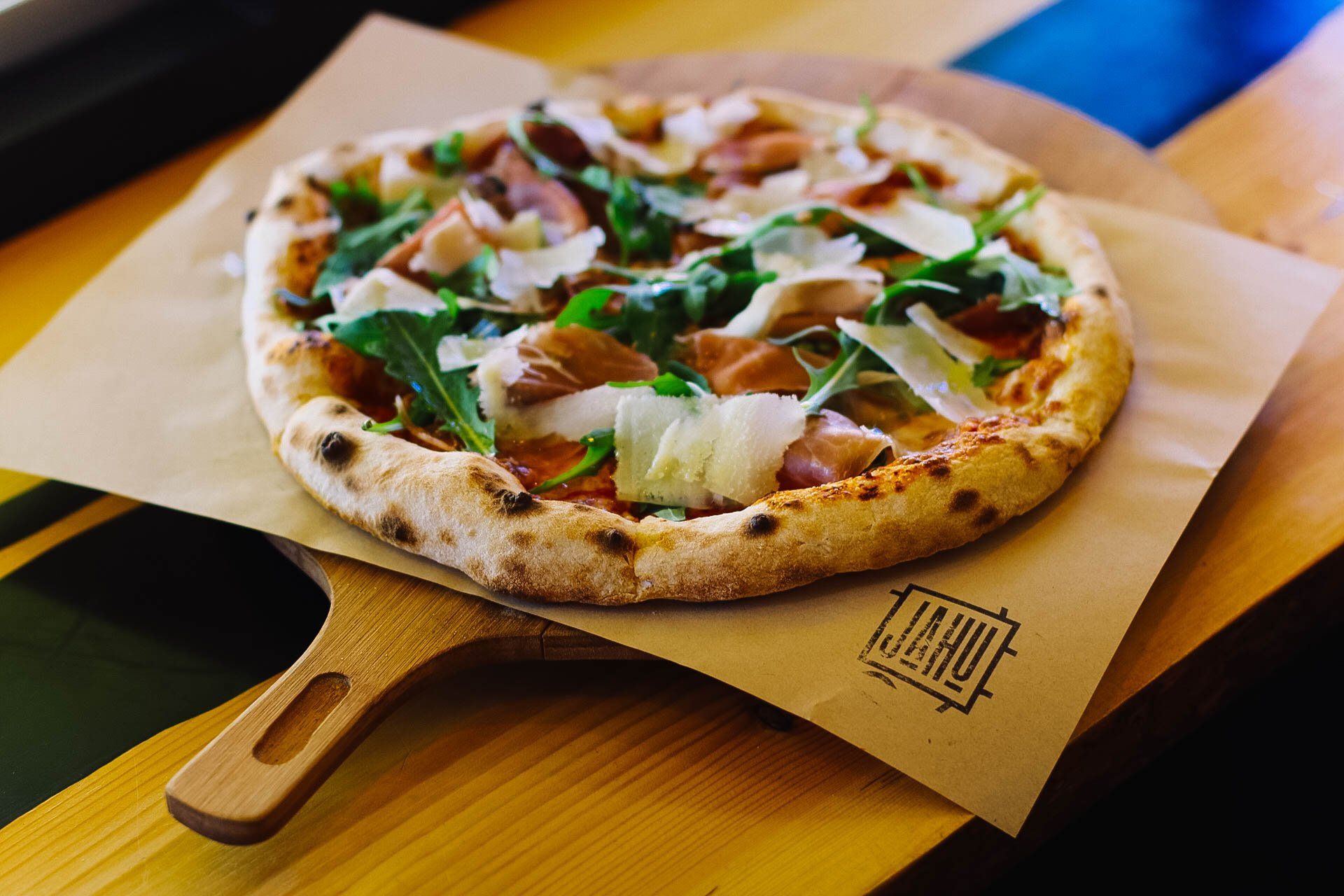 Pizza mit Rucola, Prosciutto und Parmesan auf einem Holzbrett.