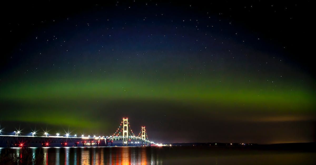 The aurora borealis is shining over a bridge over a body of water.