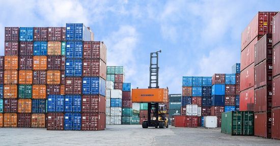 A forklift is moving a stack of shipping containers in a warehouse.