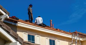 Deux hommes travaillent sur le toit d'une maison.