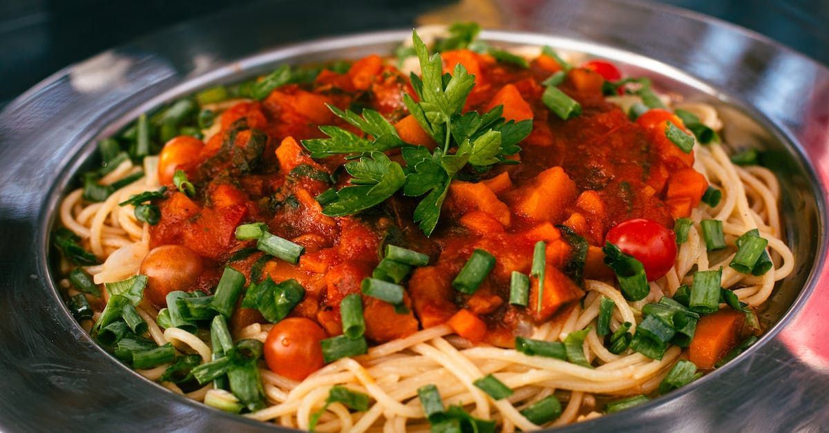 Spaghetti mit Tomatensoße, Gemüse und Kräutern in einer silbernen Schüssel.