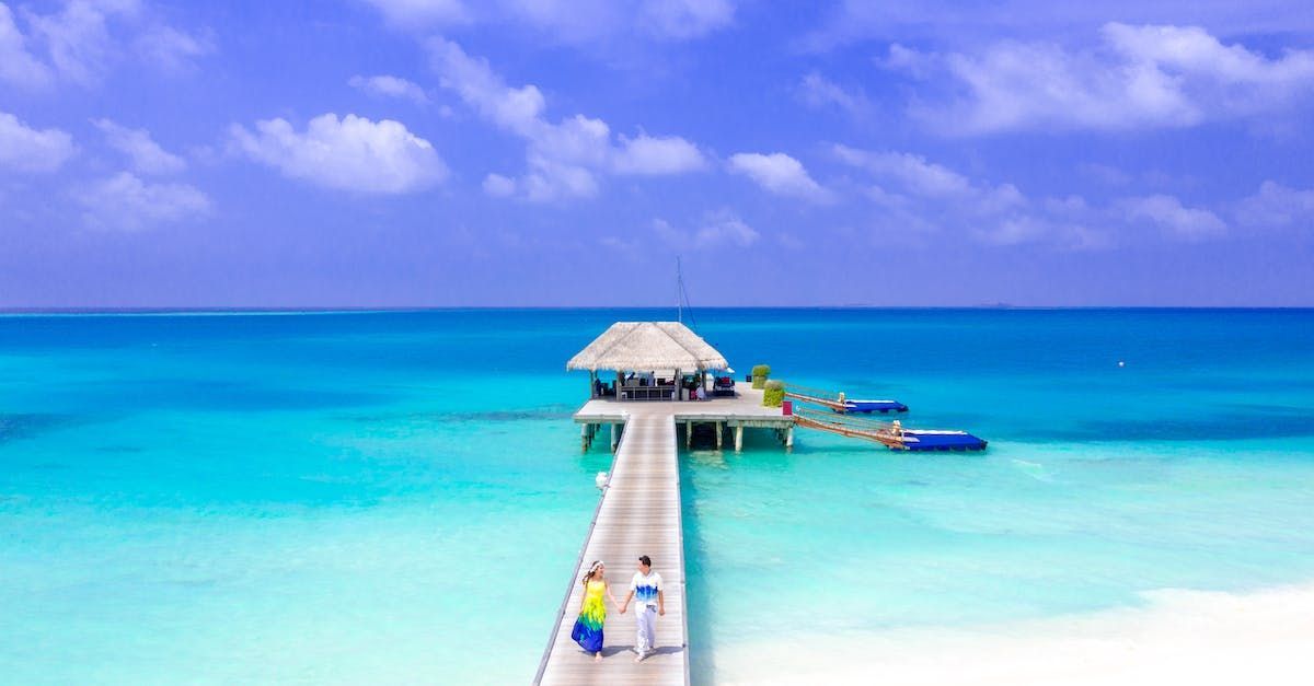 A couple is walking along a pier in the ocean.
