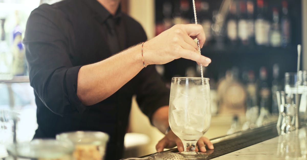 Ein Barkeeper rührt mit einem Löffel ein Getränk in einem Glas um.