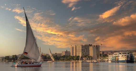 Sailboats gliding on the Nile River at sunset, with a cityscape in the background.