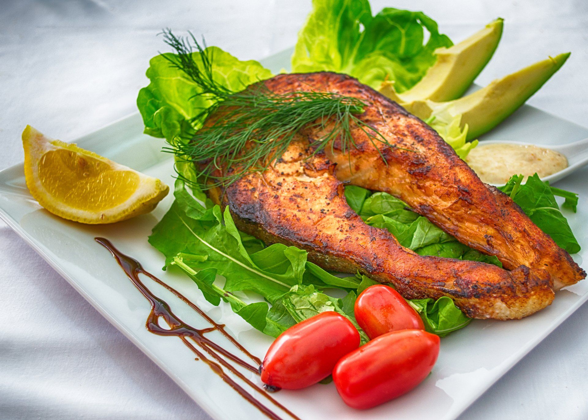 Ein weißer Teller mit einem Stück Lachs, Avocado und Tomaten