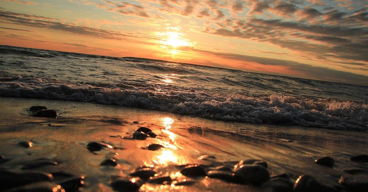 The sun is setting over the ocean and the waves are crashing on the beach.