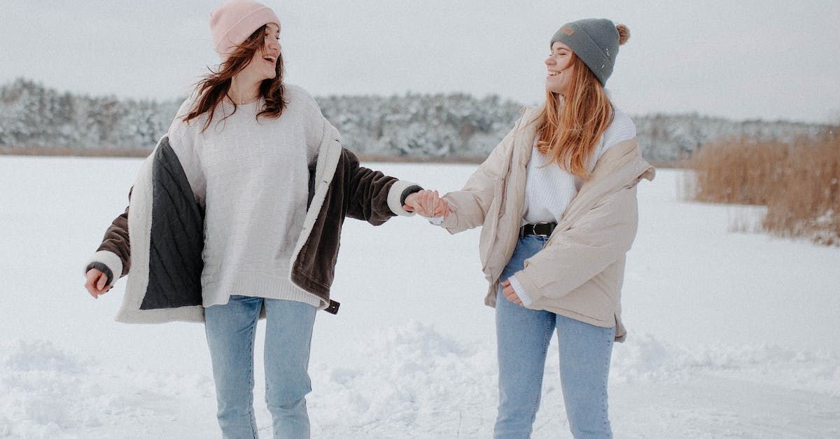Zwei Menschen in Winterkleidung halten Händchen und lächeln in einer schneebedeckten Landschaft.