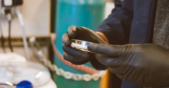 A person wearing black gloves is holding a piece of metal.