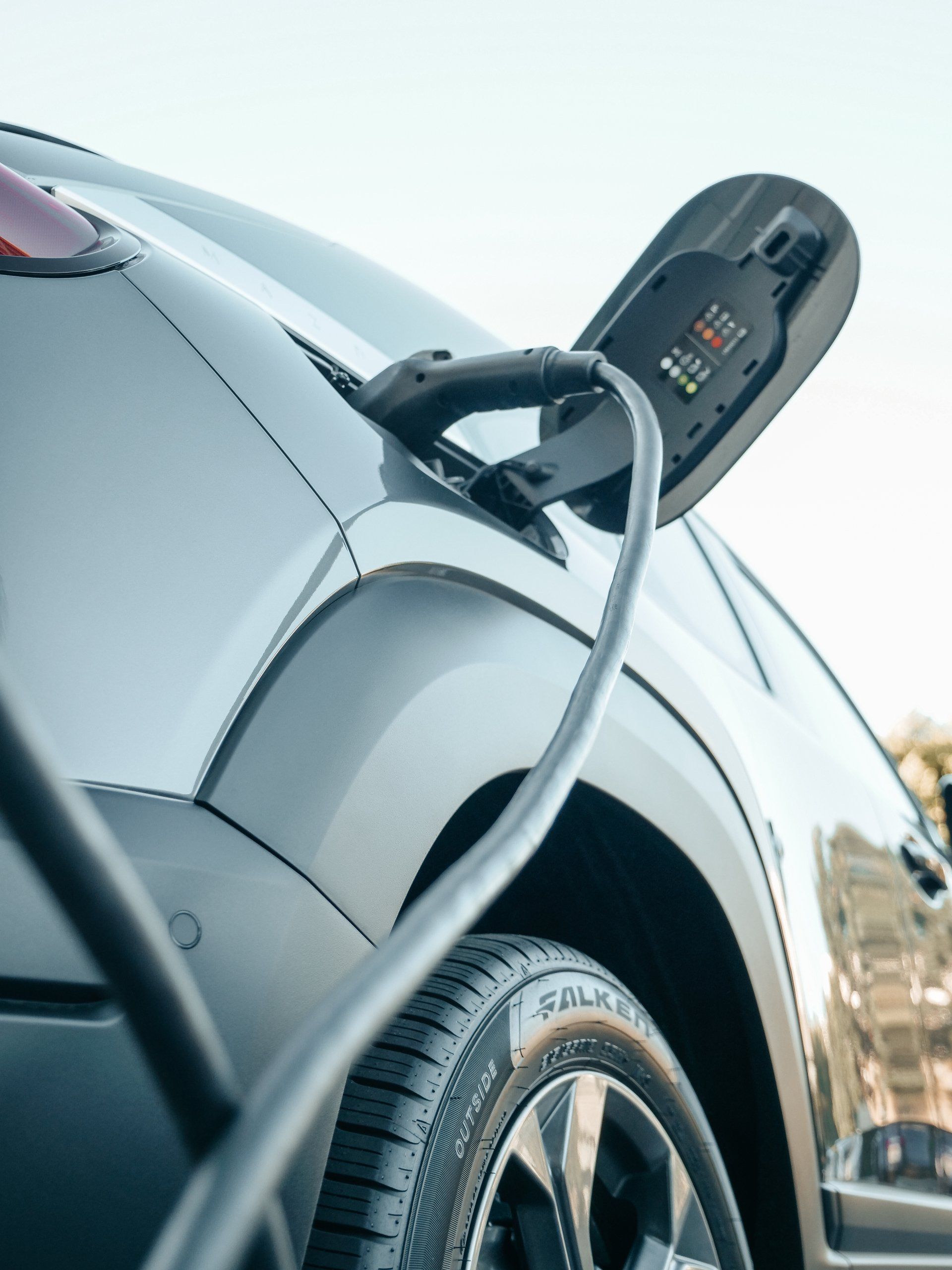 Electric vehicle charging, grey car with a charging cable plugged in, tire visible.