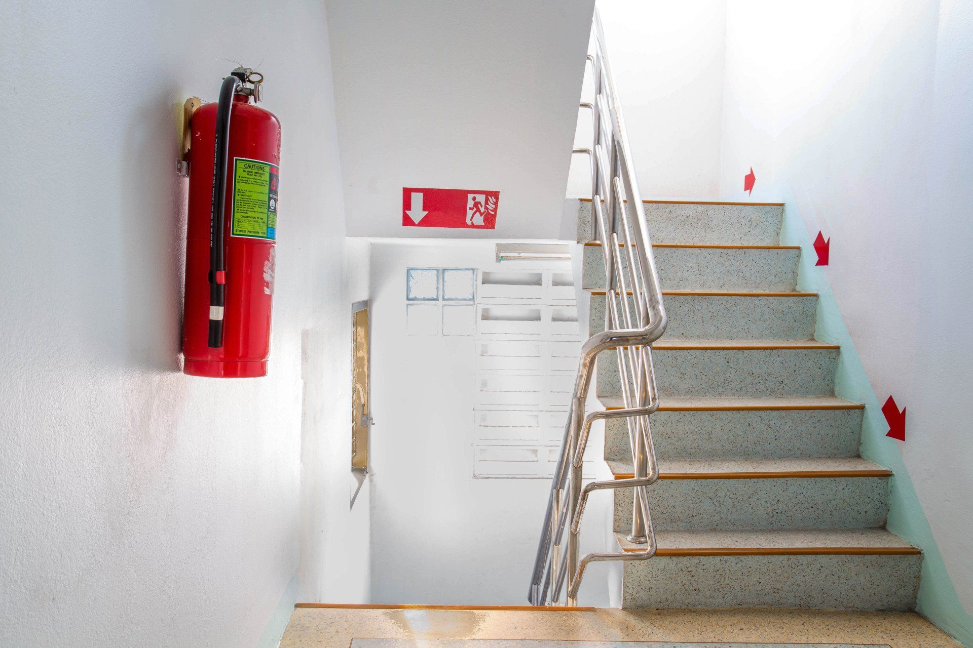 Extincteur et cage d'escalier avec panneaux de sortie rouges.