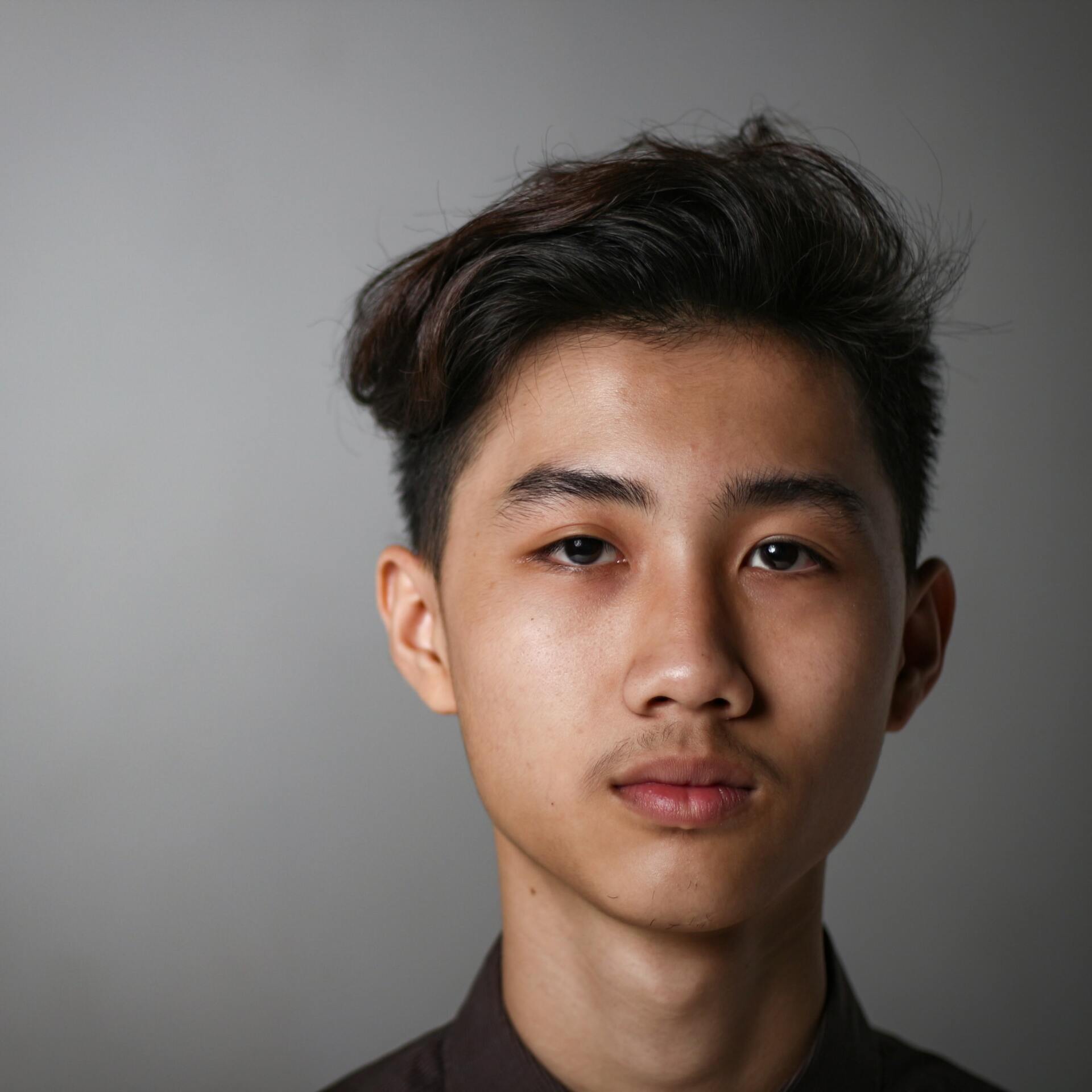 Une jeune personne aux cheveux foncés regarde directement le spectateur sur un fond gris.